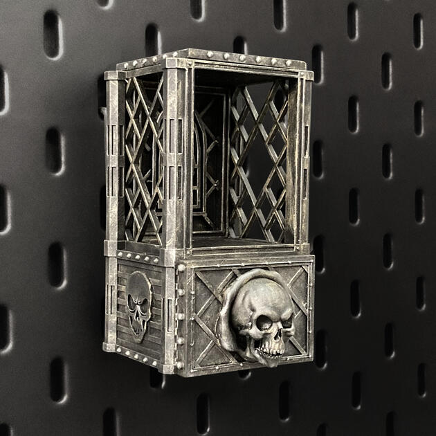 Hand-painted weathered iron skull dice box with open storage drawer, mounted on an IKEA SKÅDIS pegboard for TTRPG miniature display.