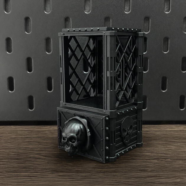 Hand-painted weathered iron skull dice box with open storage drawer, mounted on an IKEA SKÅDIS pegboard for TTRPG miniature display.