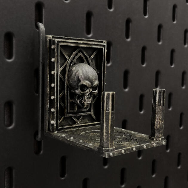Hand-painted weathered iron skull dice box, mounted on an IKEA SKÅDIS pegboard for TTRPG miniature display.