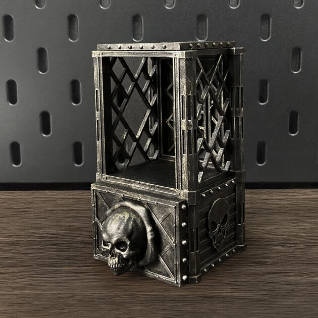 Hand-painted weathered iron skull dice box with open storage drawer, mounted on an IKEA SKÅDIS pegboard for TTRPG miniature display.